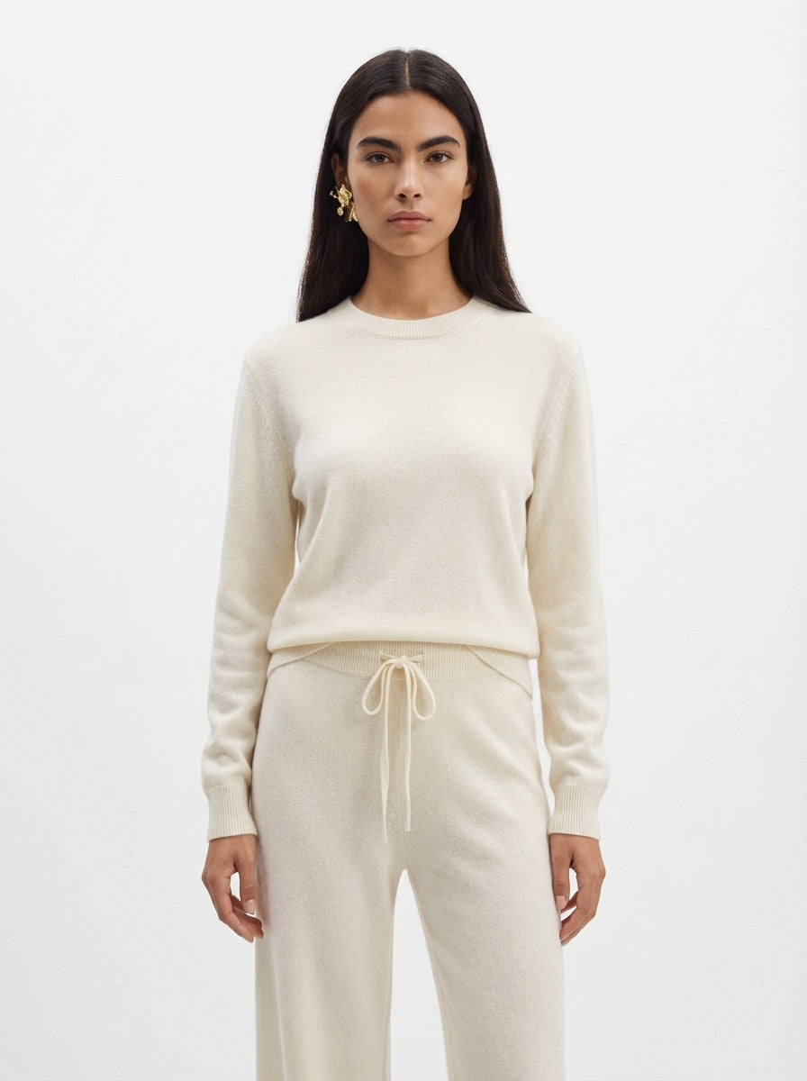 Woman wearing a cream-colored sweater and pants on a white background