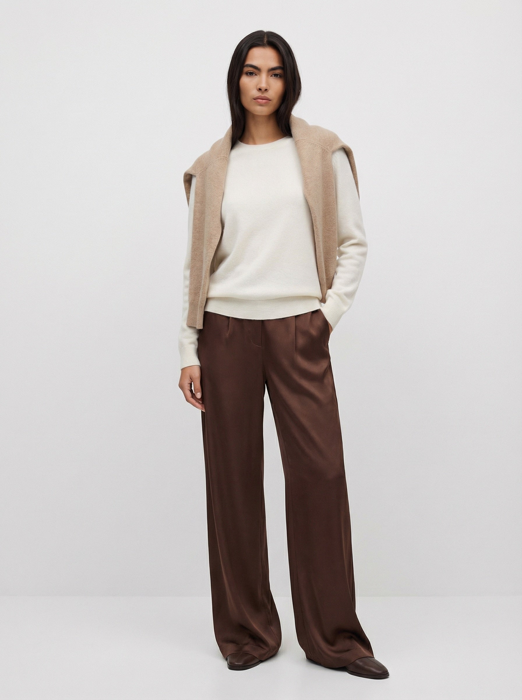 Woman wearing a beige cardigan, white top, and brown pants on a white background